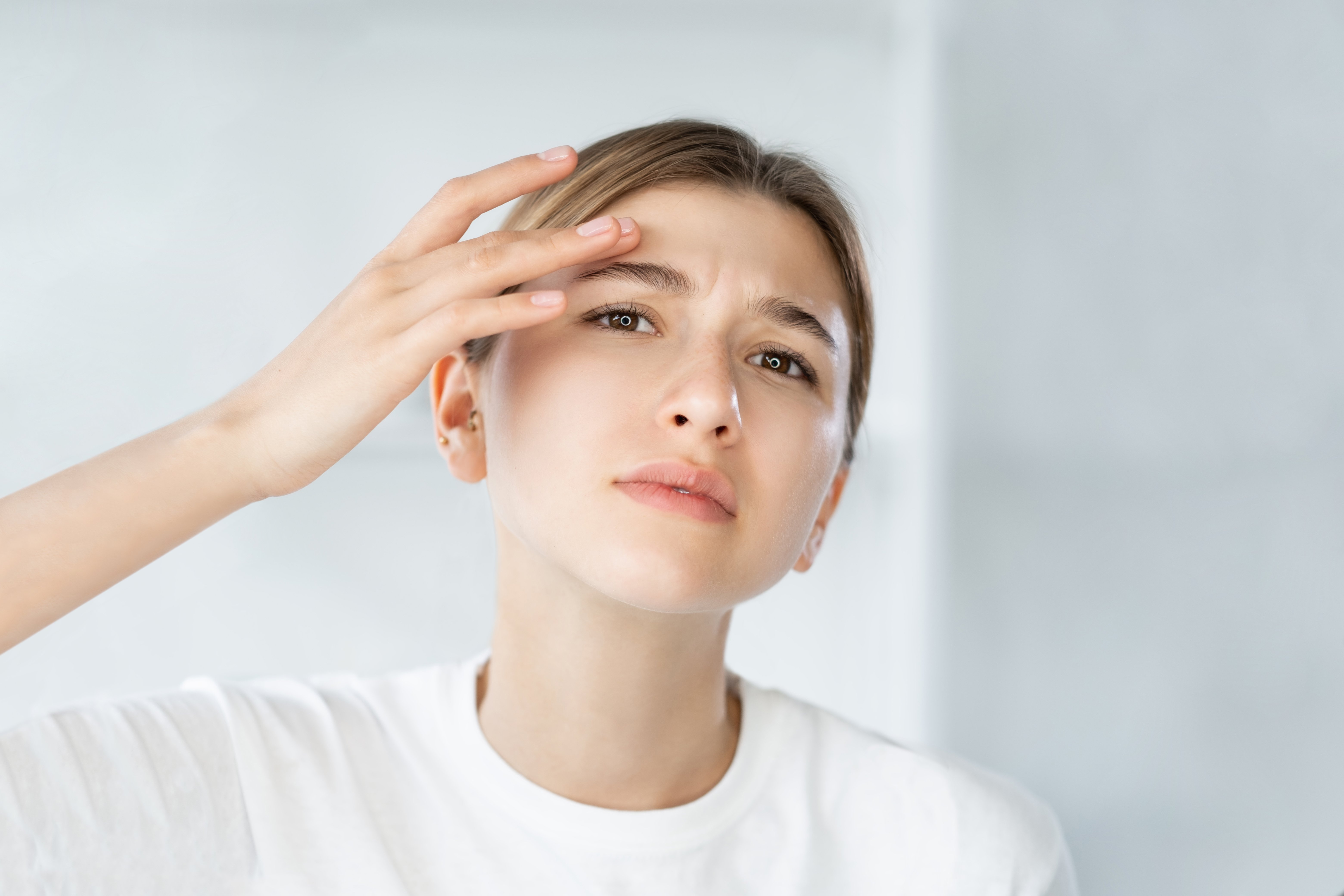 Frau schaut prüfend in einen Spiegel und überprüft mit der Hand die Augen- und Stirnpartie auf Neurodermitis Symptome